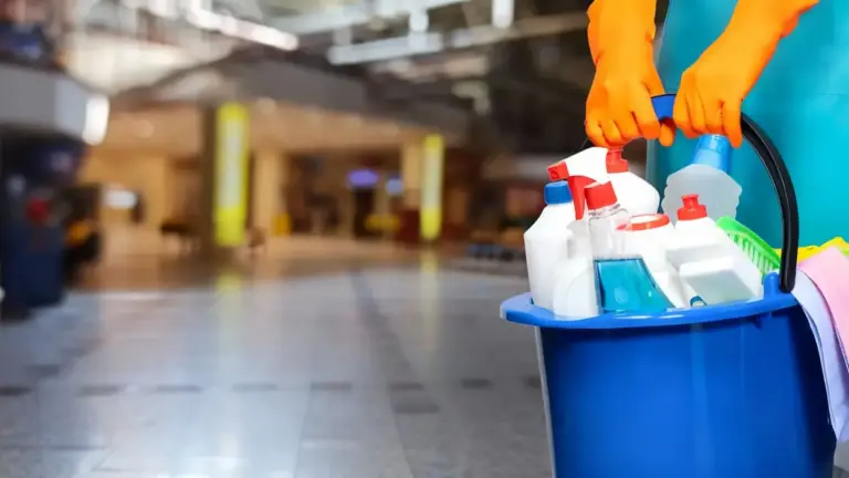 Persona con guanti arancioni tiene un secchio con prodotti per la pulizia in un edificio