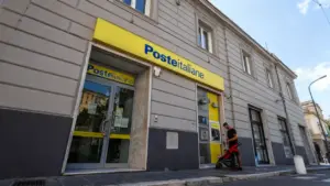 Ufficio di Poste Italiane con sportelli automatici e una persona con passeggino sul marciapiede