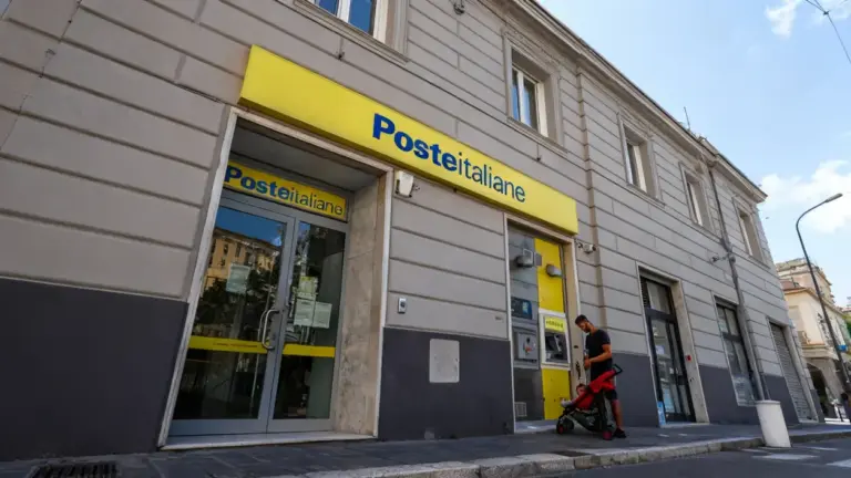 Ufficio di Poste Italiane con sportelli automatici e una persona con passeggino sul marciapiede