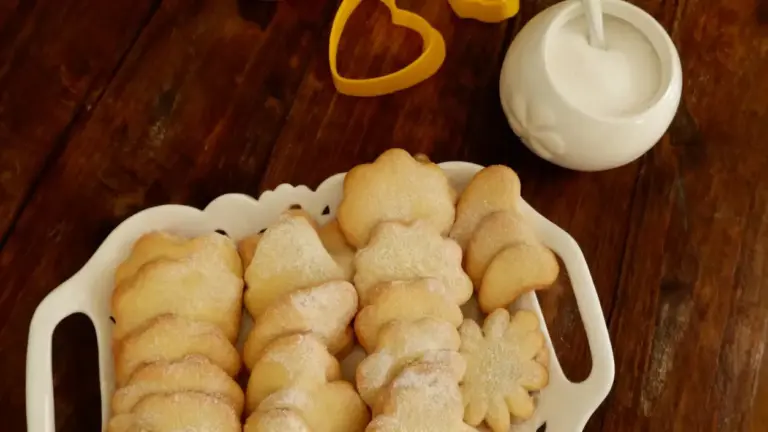 Biscotti fatti in casa disposti su un vassoio bianco con zucchero e formine sul tavolo di legno