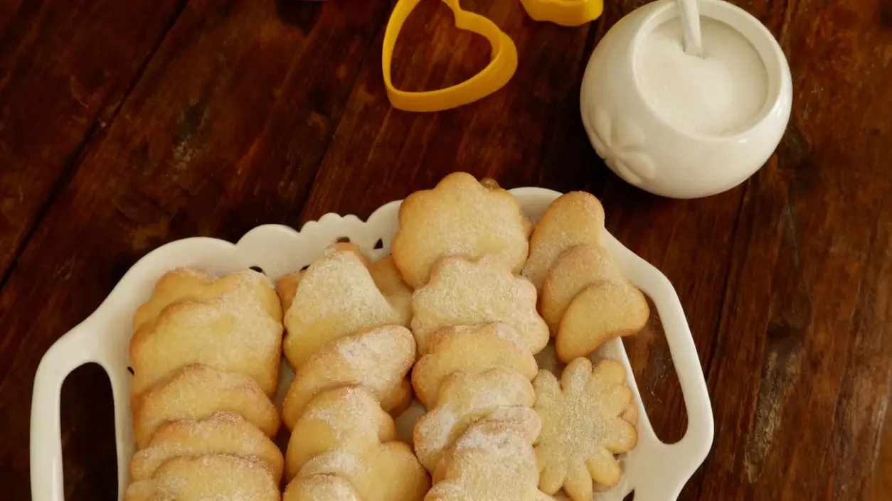 Biscotti fatti in casa disposti su un vassoio bianco con zucchero e formine sul tavolo di legno