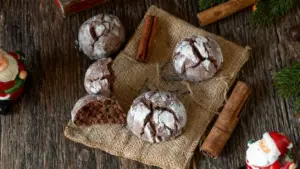 Biscotti al cacao spolverati di zucchero a velo su tovaglietta rustica con stecche di cannella