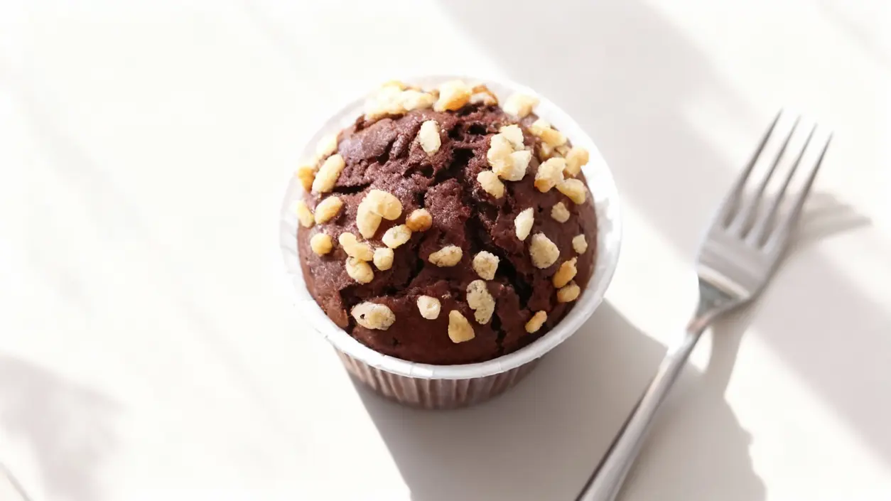 Muffin al cioccolato con granella su un tavolo chiaro accanto a una forchetta