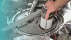 Una mano rimuove il filtro da una lavastoviglie per pulirlo facilmente