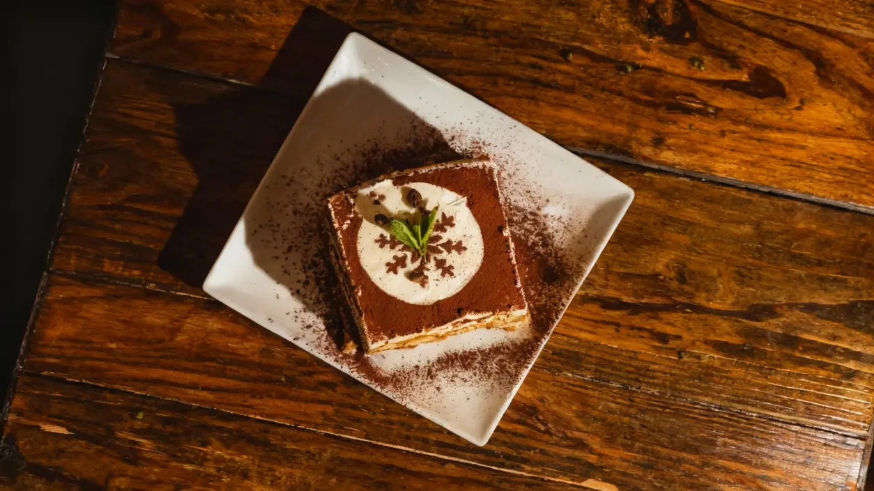 Dessert al cacao su piatto quadrato bianco con decorazione in crema e fogliolina