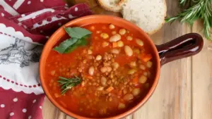 Zuppa cremosa di legumi in ciotola di terracotta con foglie di alloro e rosmarino